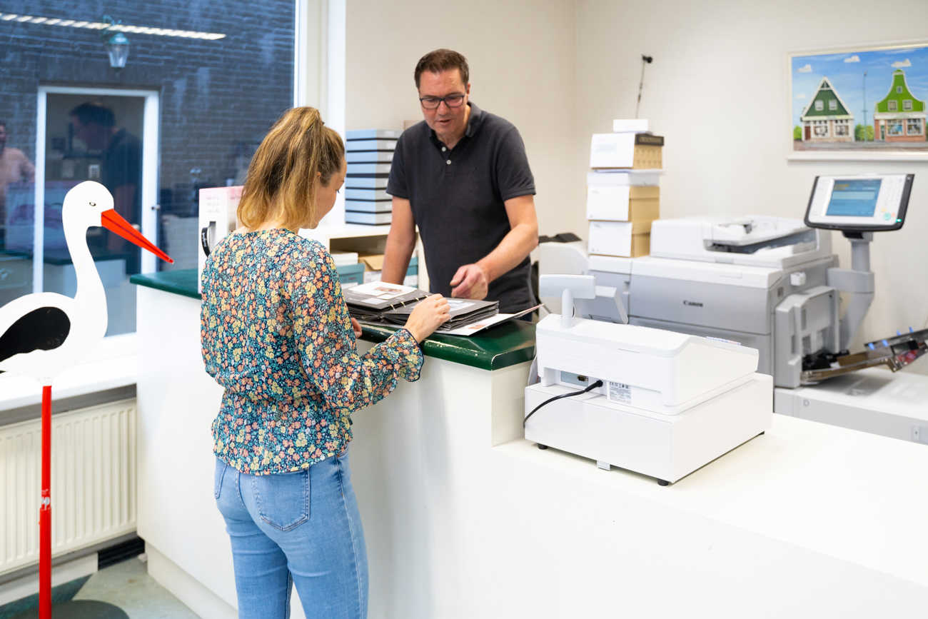Klant achter balie in Drukkerij Zaansprint die door inspiratie boeken aan het bladeren is